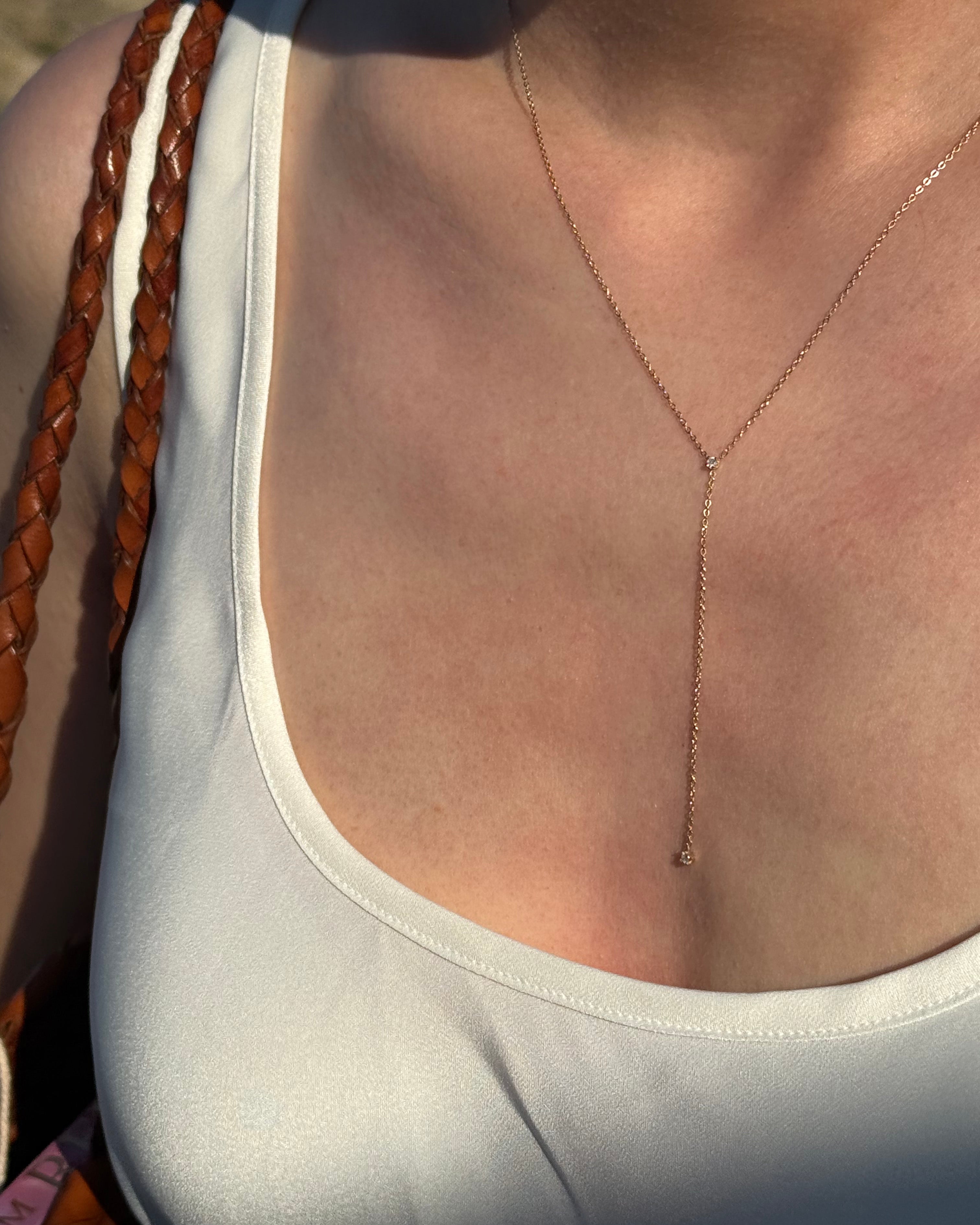 Close-up of a person wearing a thin gold necklace with a neutral background