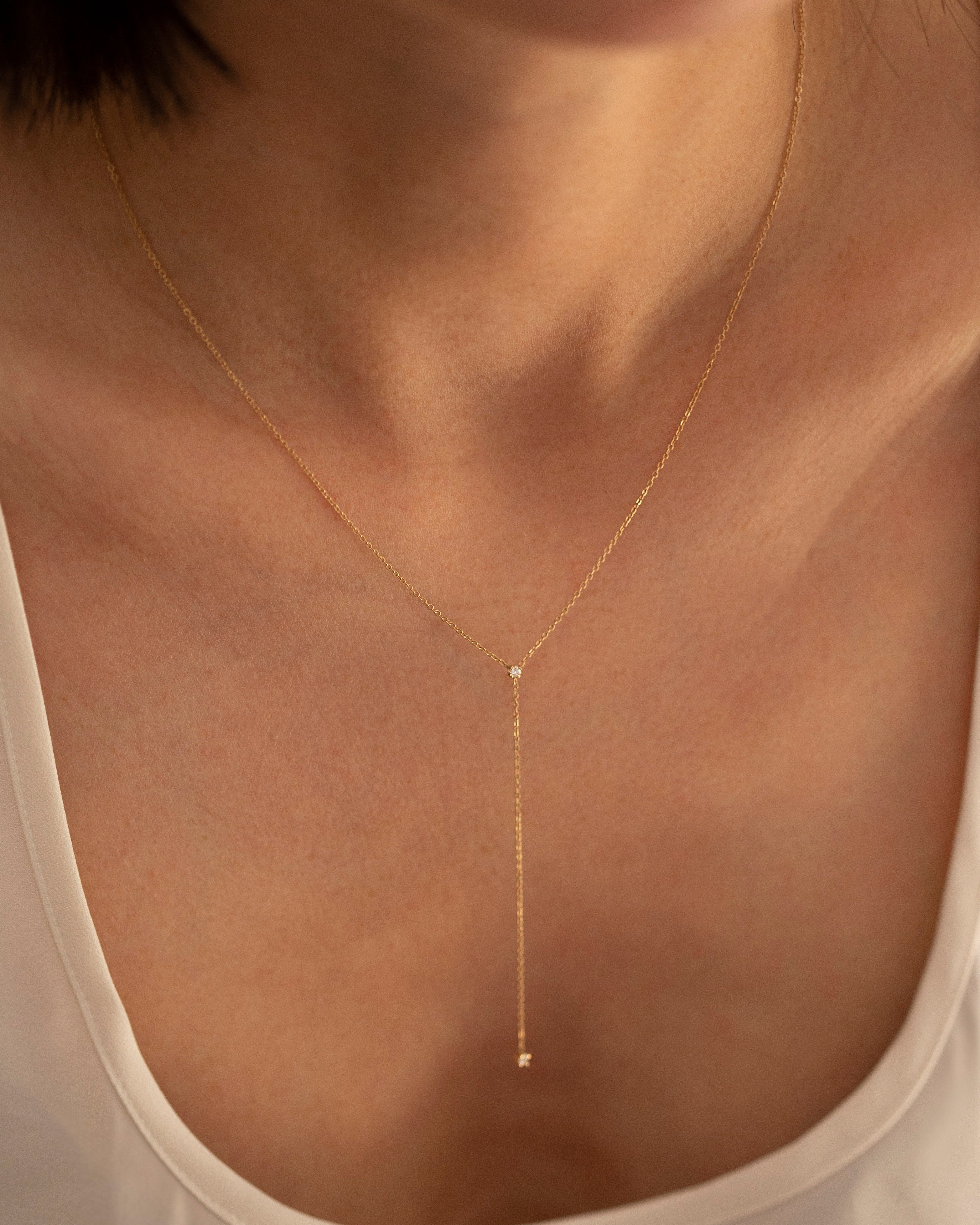 Gold necklace with a small pendant on a person wearing a beige top.