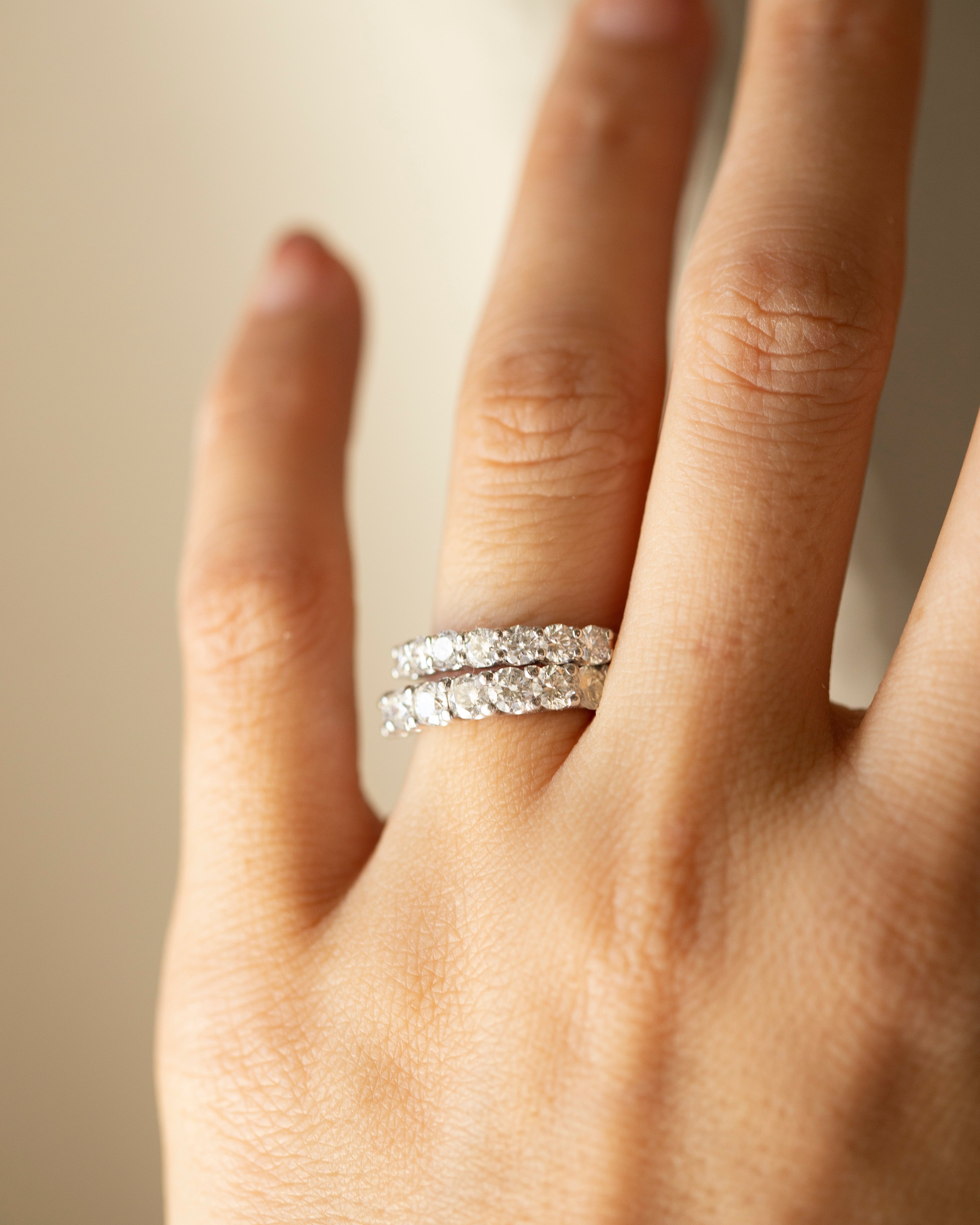 Hand wearing a silver ring with a diamond band on a neutral background