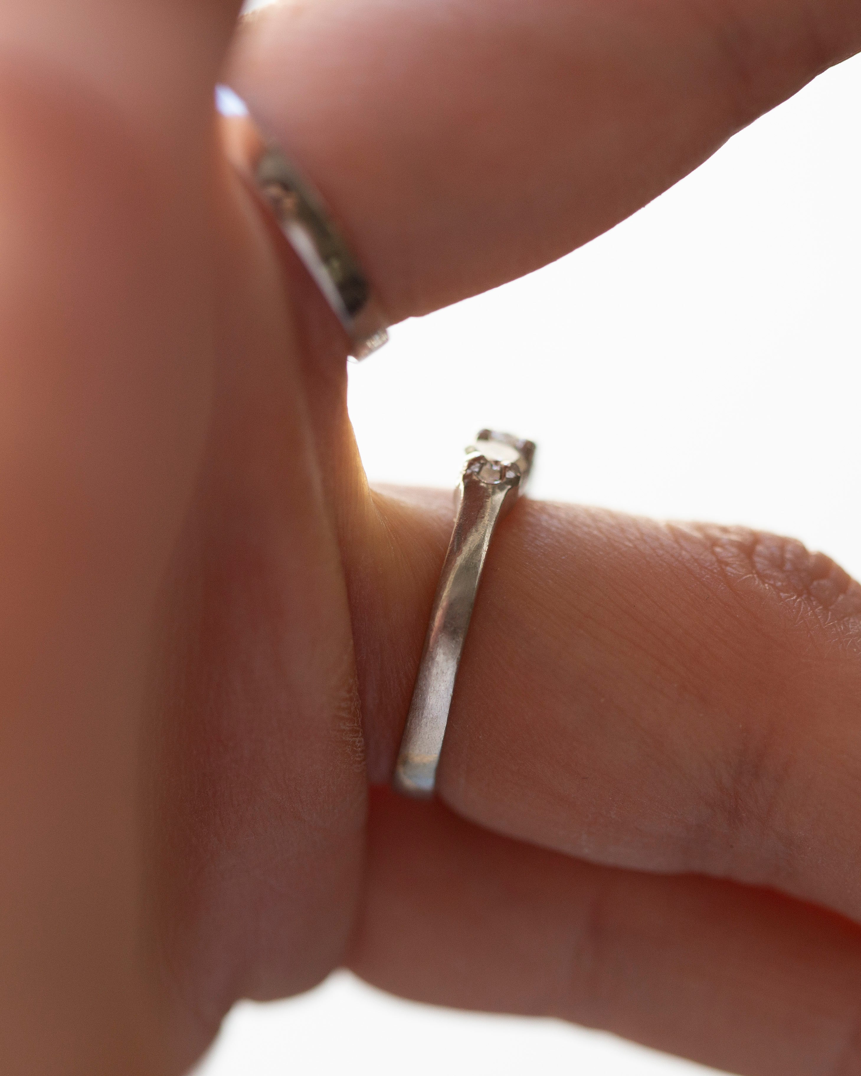 Close-up of a hand wearing two silver rings on a light background