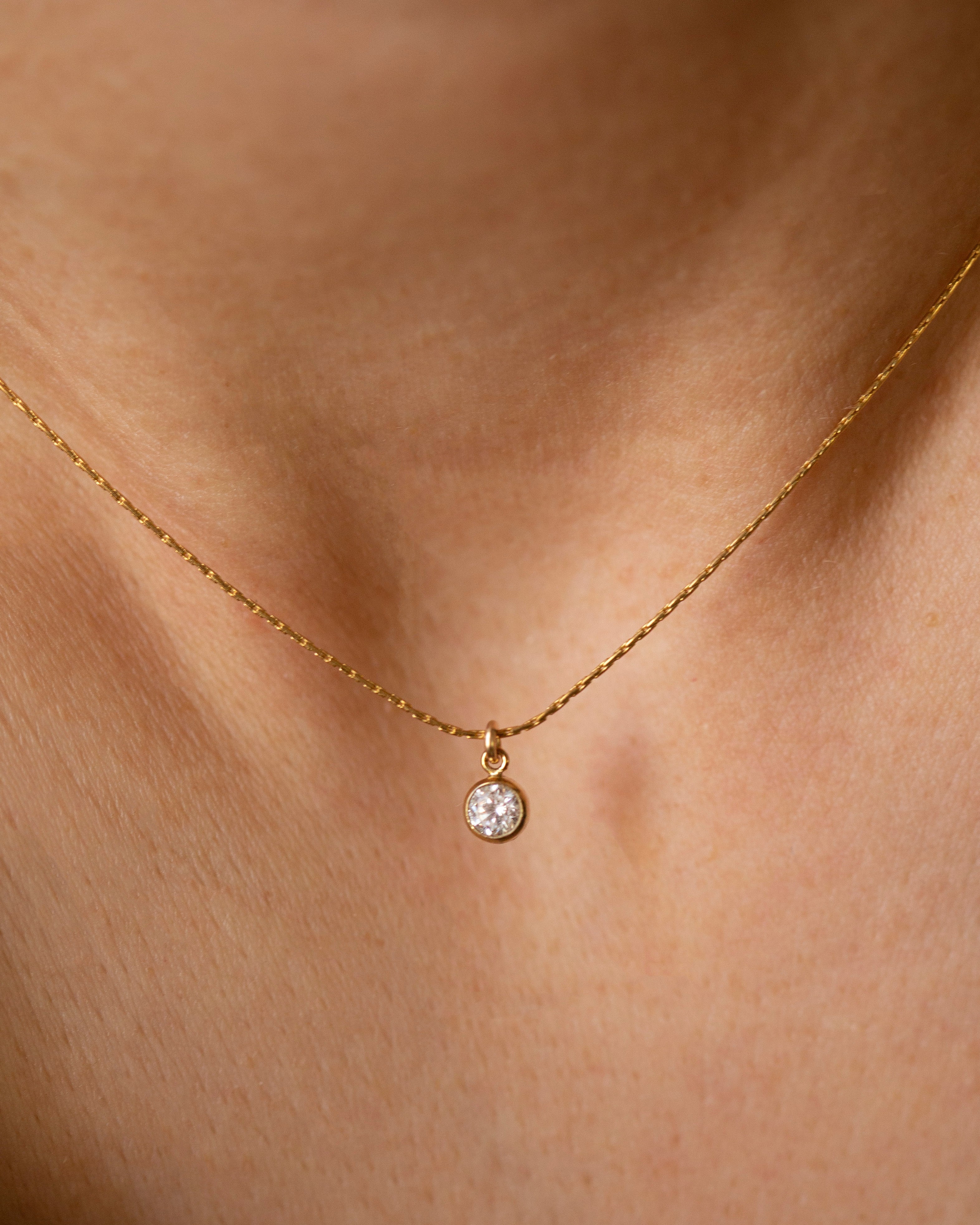 Gold necklace with a small round pendant on a person's neck