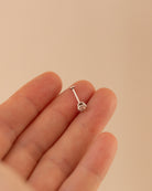 Silver barbell earring on a hand against a beige background