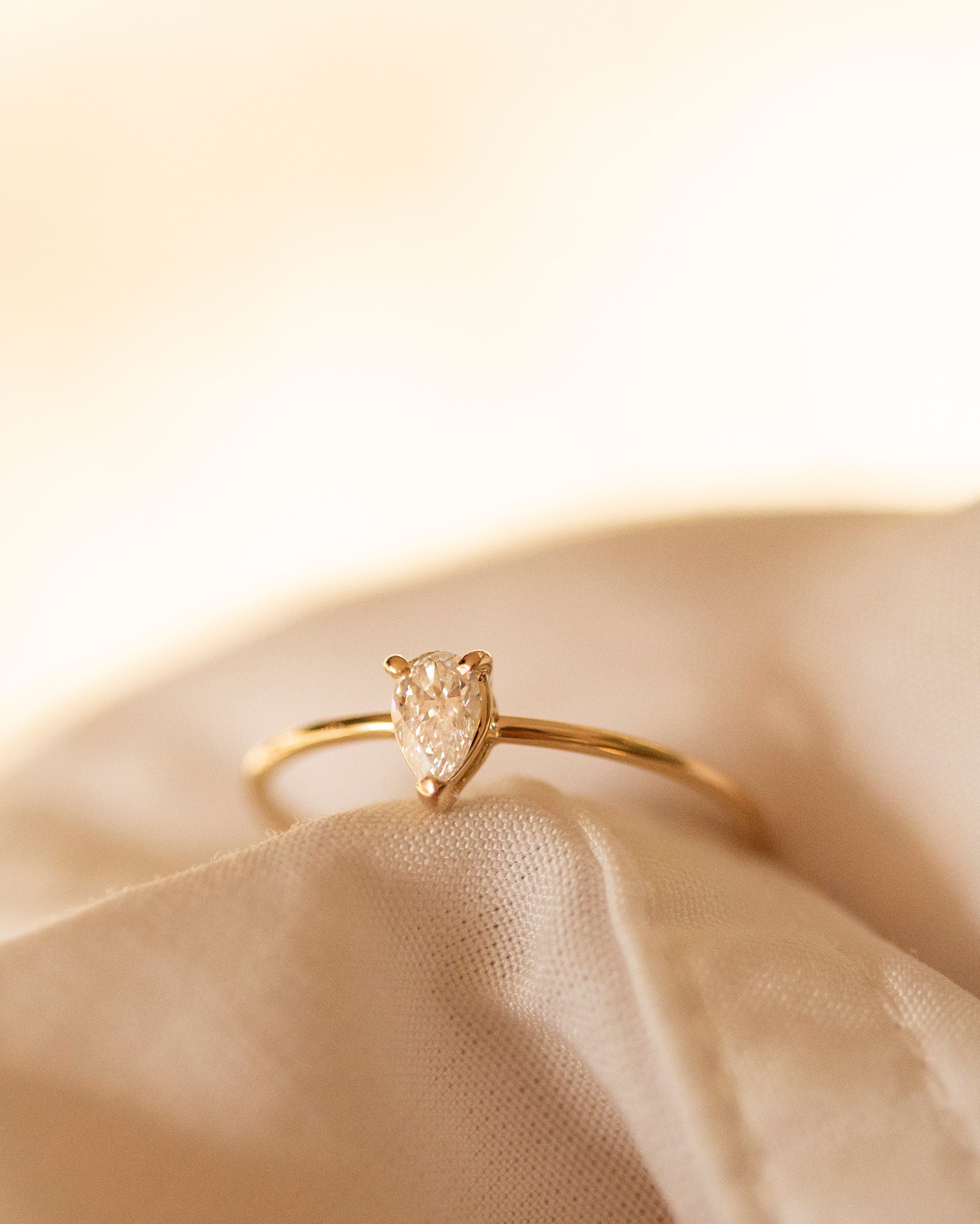 Gold ring with a heart-shaped diamond on a beige fabric background