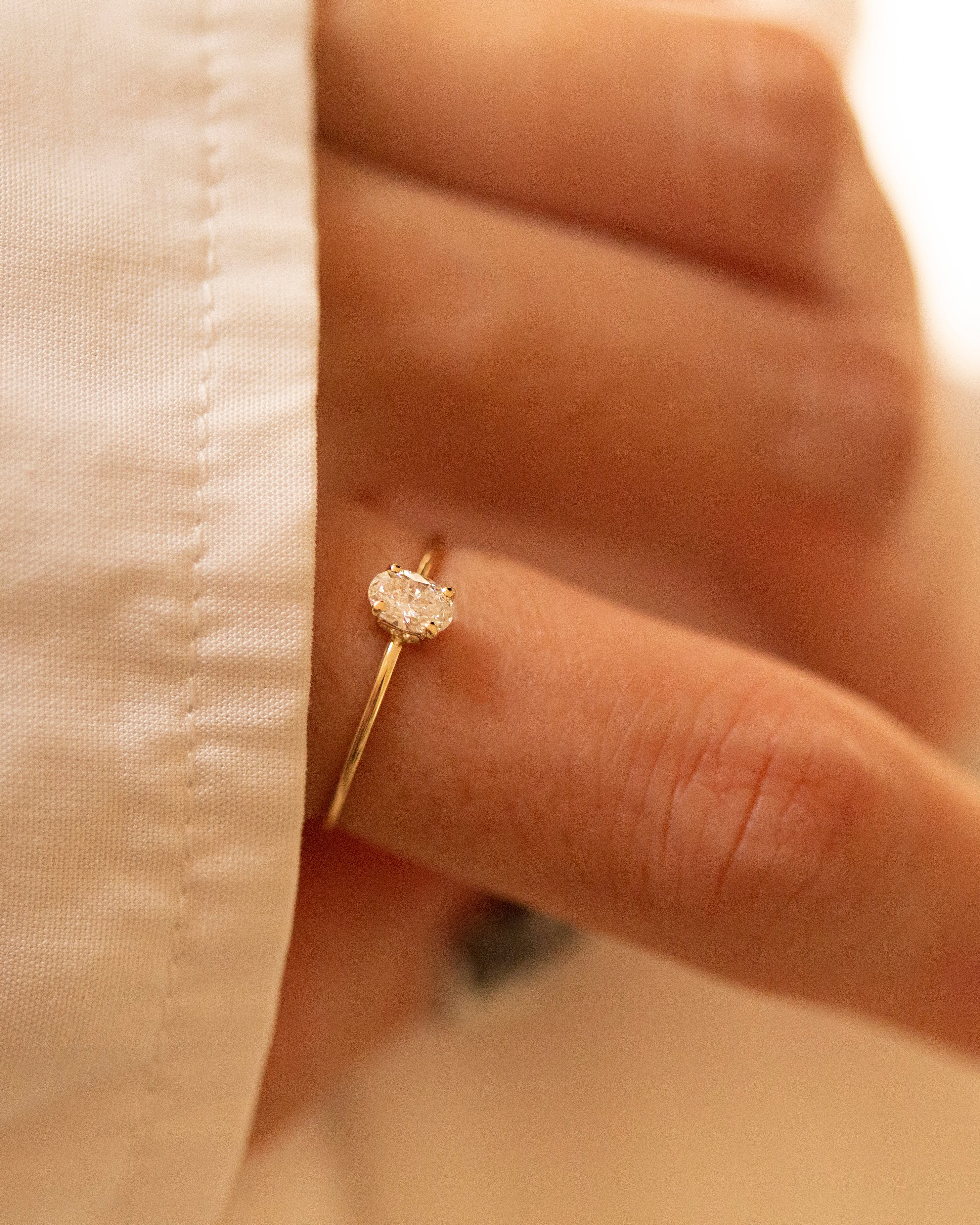Gold ring with a diamond on a person's finger against a beige fabric background