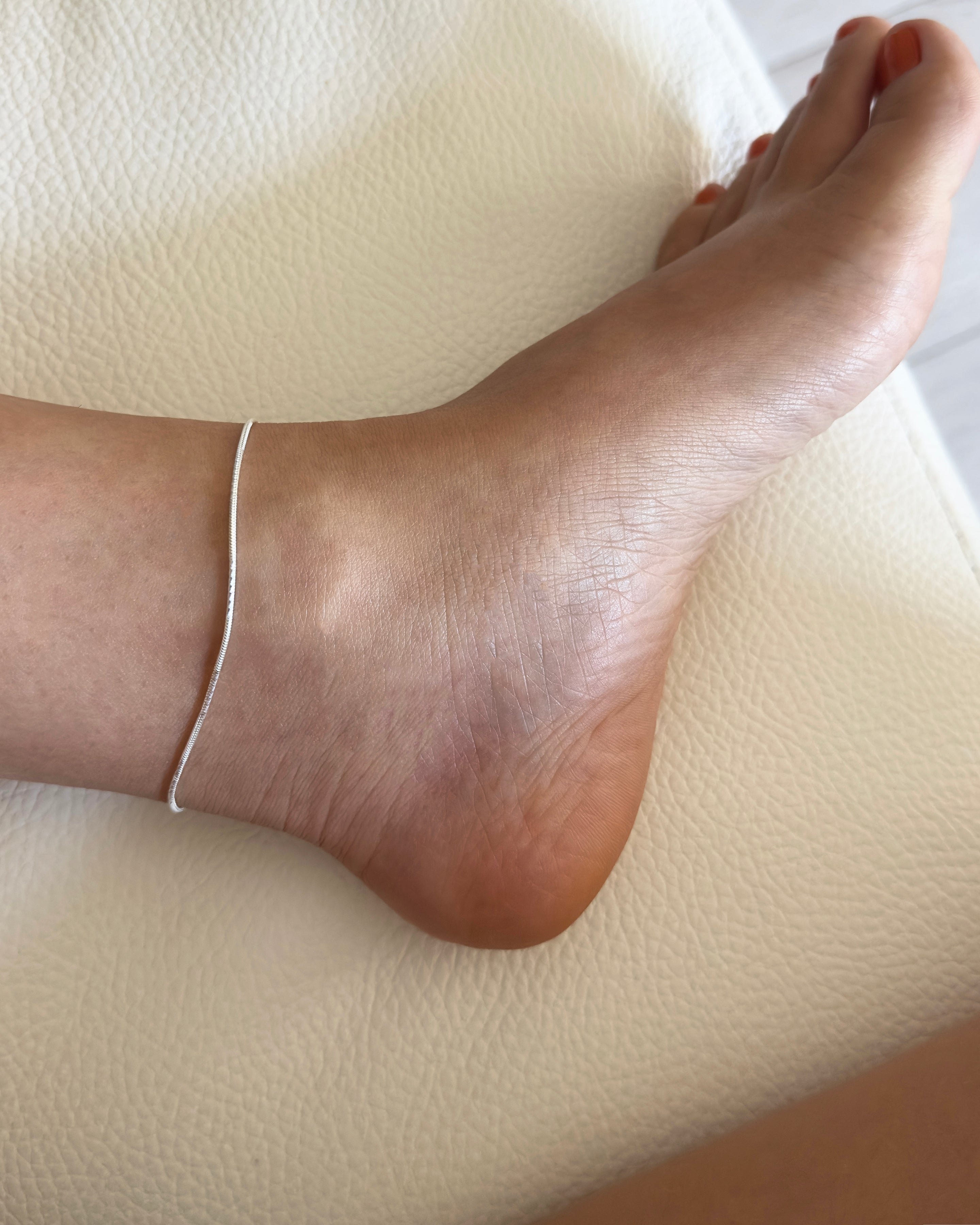 Close-up of a foot with a anklet on a light-colored surface