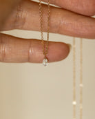 Gold necklace with a diamond pendant held between fingers on a neutral background