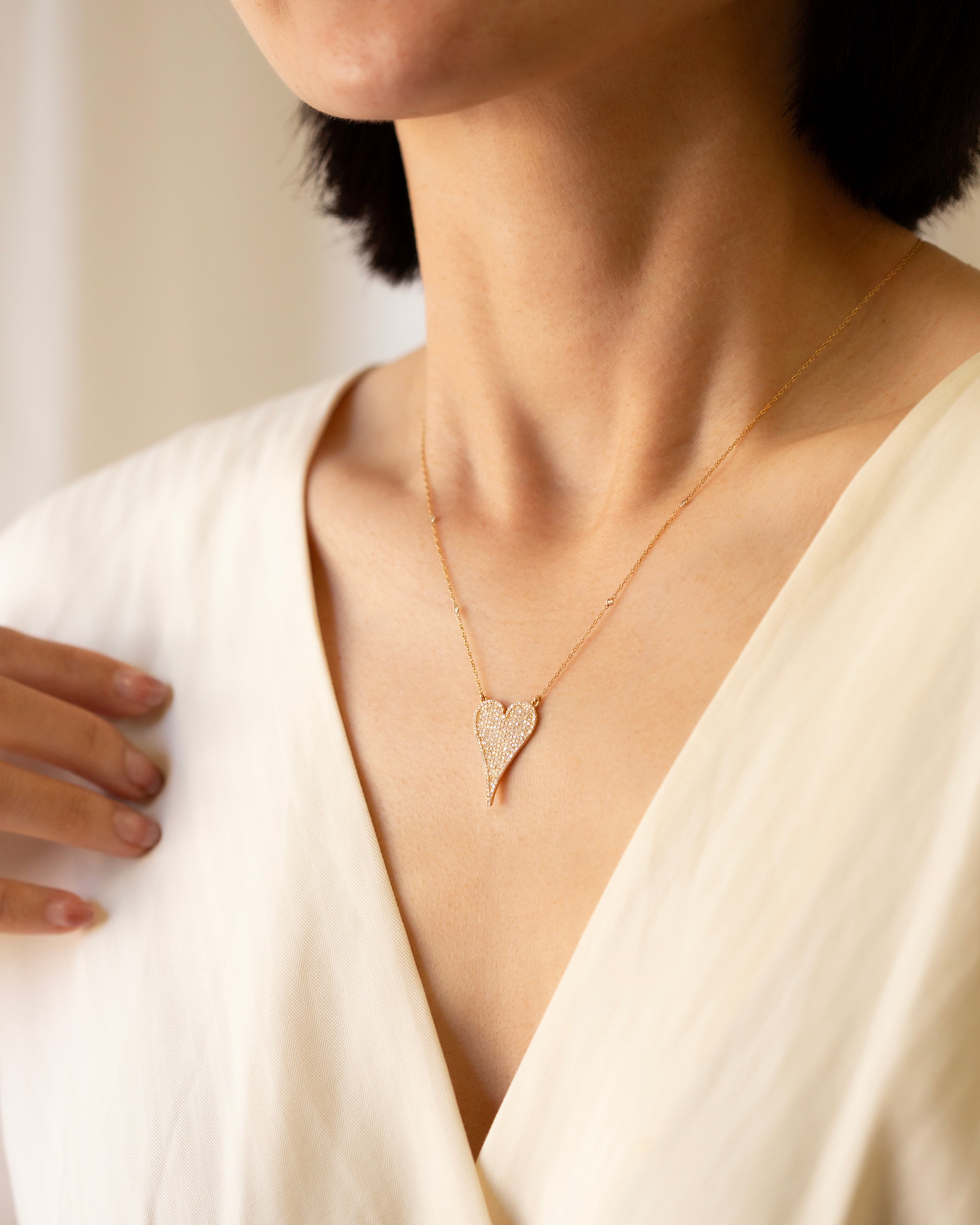 Person wearing a delicate gold necklace with a heart pendant against a neutral background