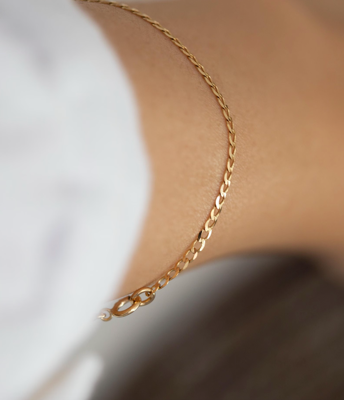 Gold necklace on a person wearing a white shirt