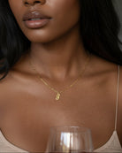 Woman wearing a gold necklace with a small pendant, holding a glass of wine.