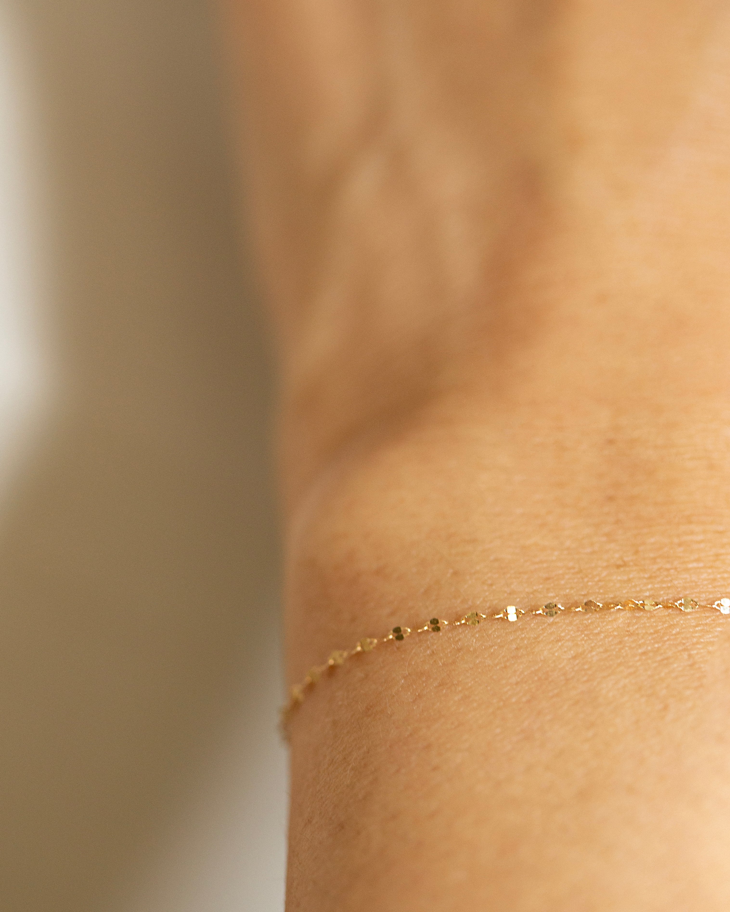 Gold bracelet on a person's ankle with a neutral background