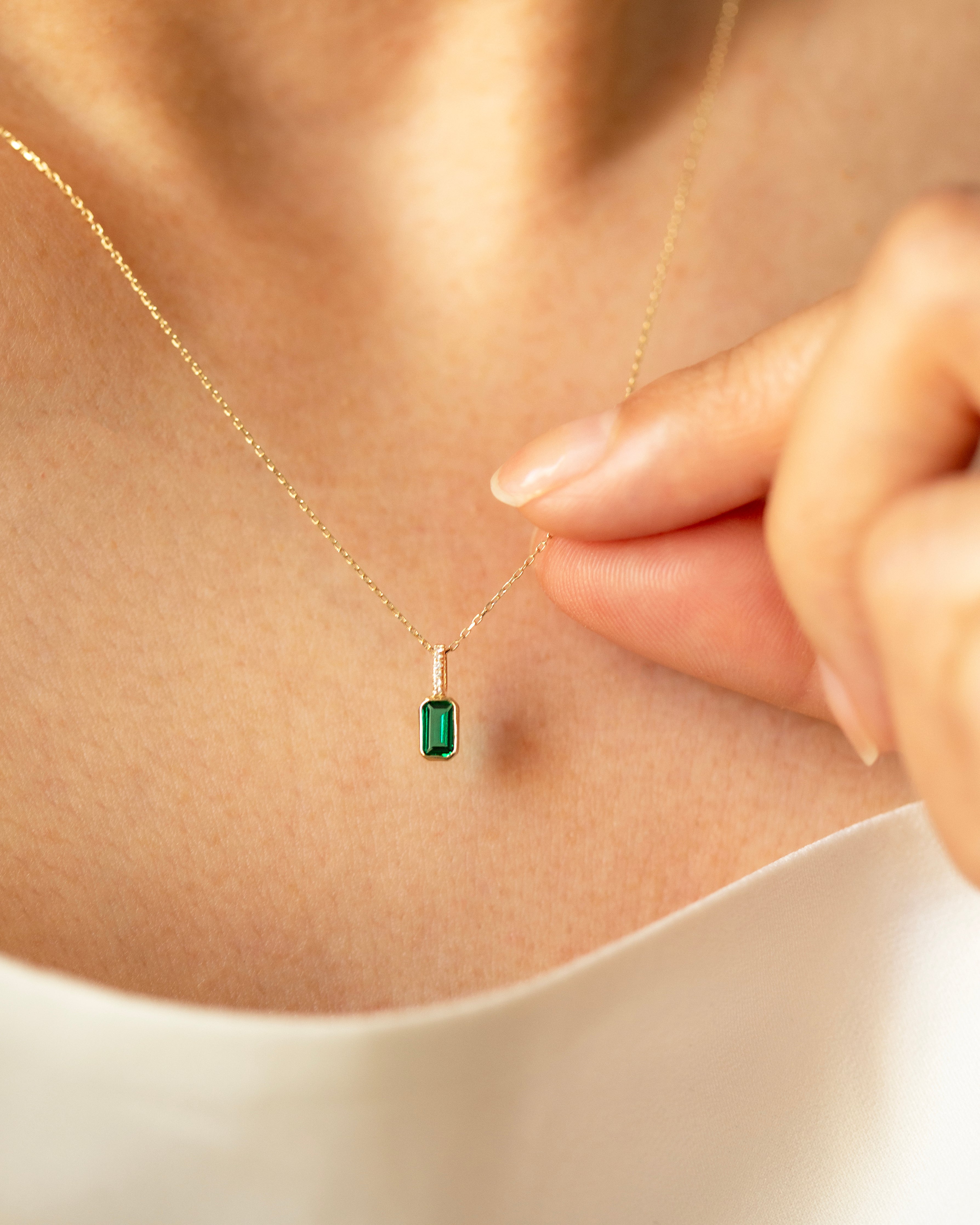 Gold necklace with a green gemstone pendant being adjusted on a person's neck.