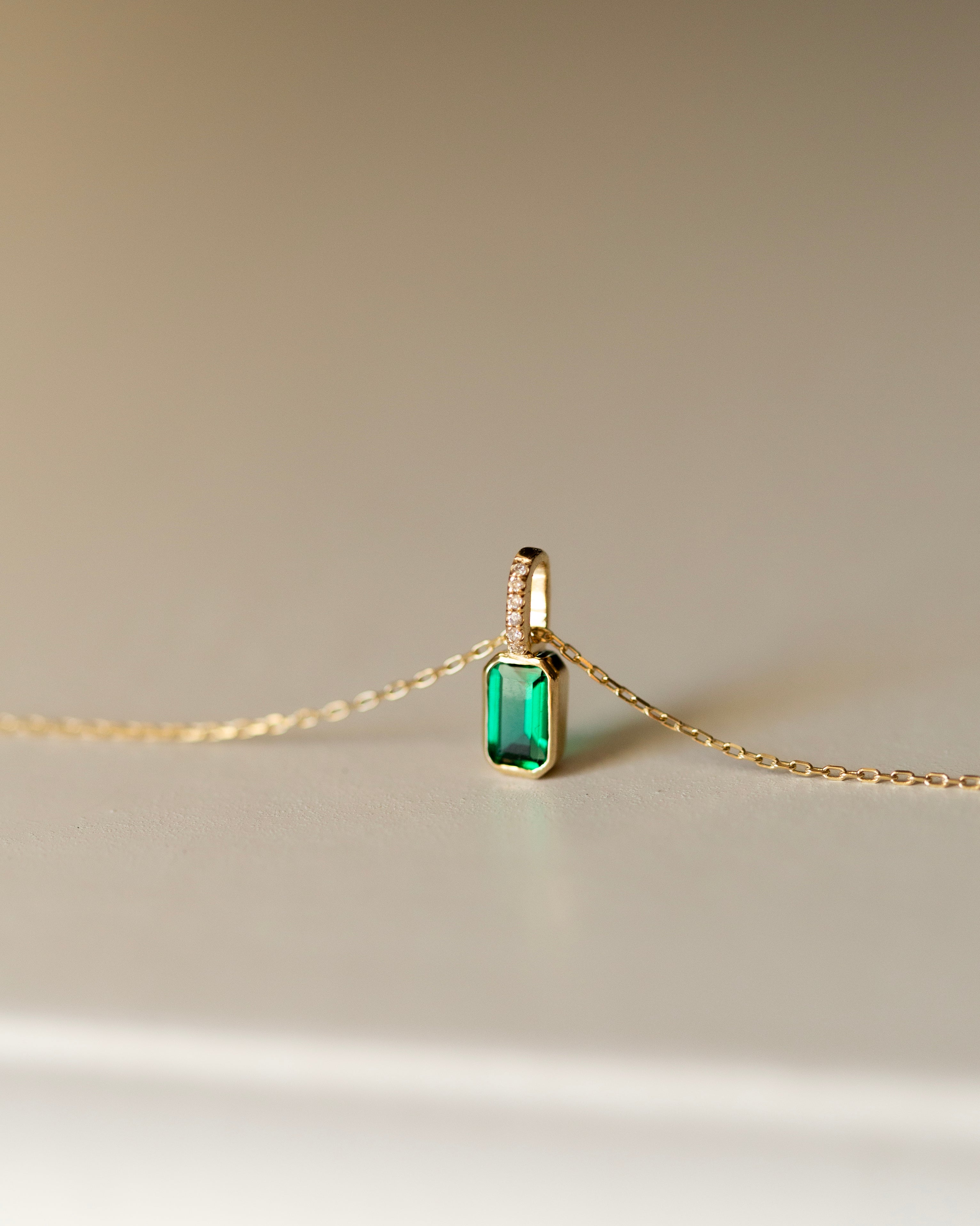 Gold necklace with a green gemstone pendant on a beige background
