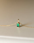 Gold necklace with a green gemstone pendant on a beige background