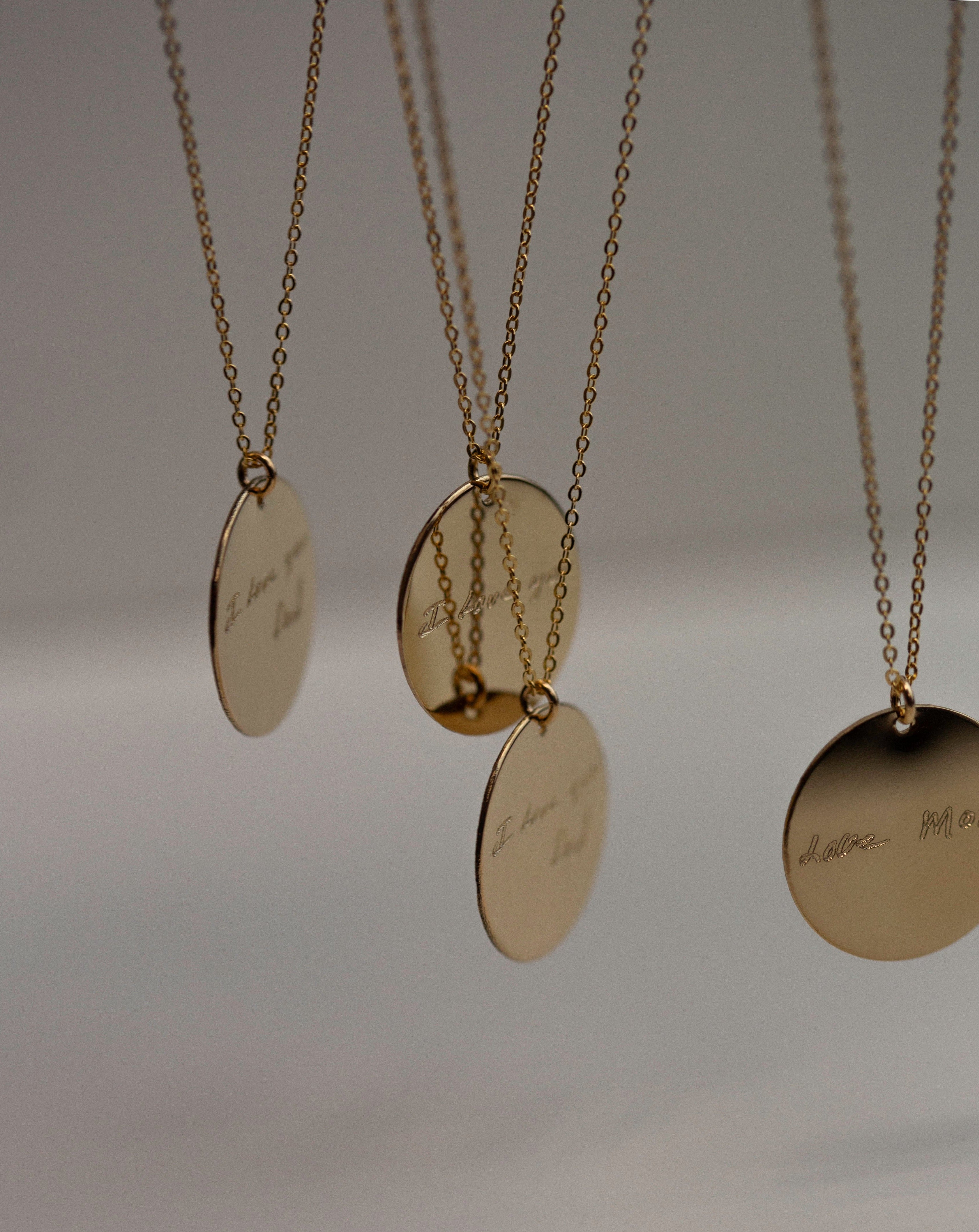 A gold chain necklace with a round, gold pendant.