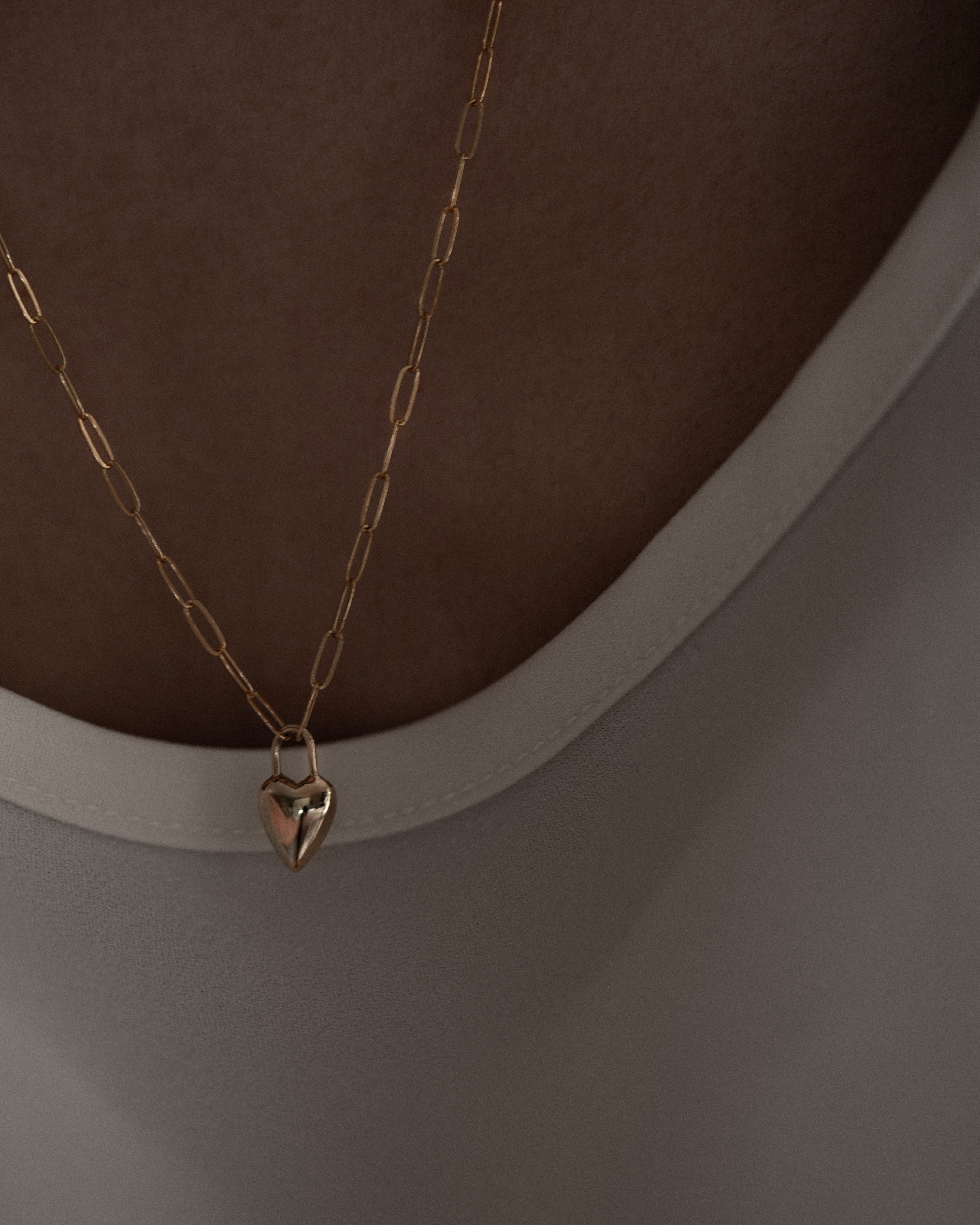 Gold necklace with a heart-shaped pendant on a plain background