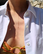 Person wearing a white shirt with a necklace, standing outdoors.