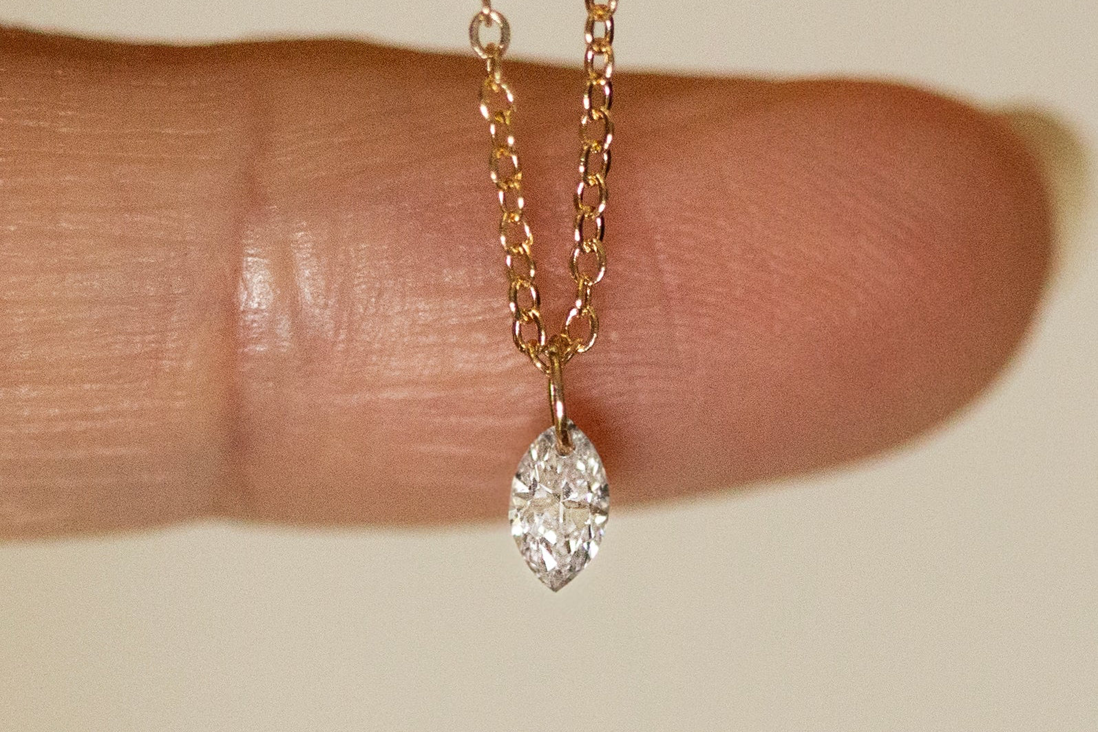 Gold necklace with a diamond pendant held between fingers on a neutral background