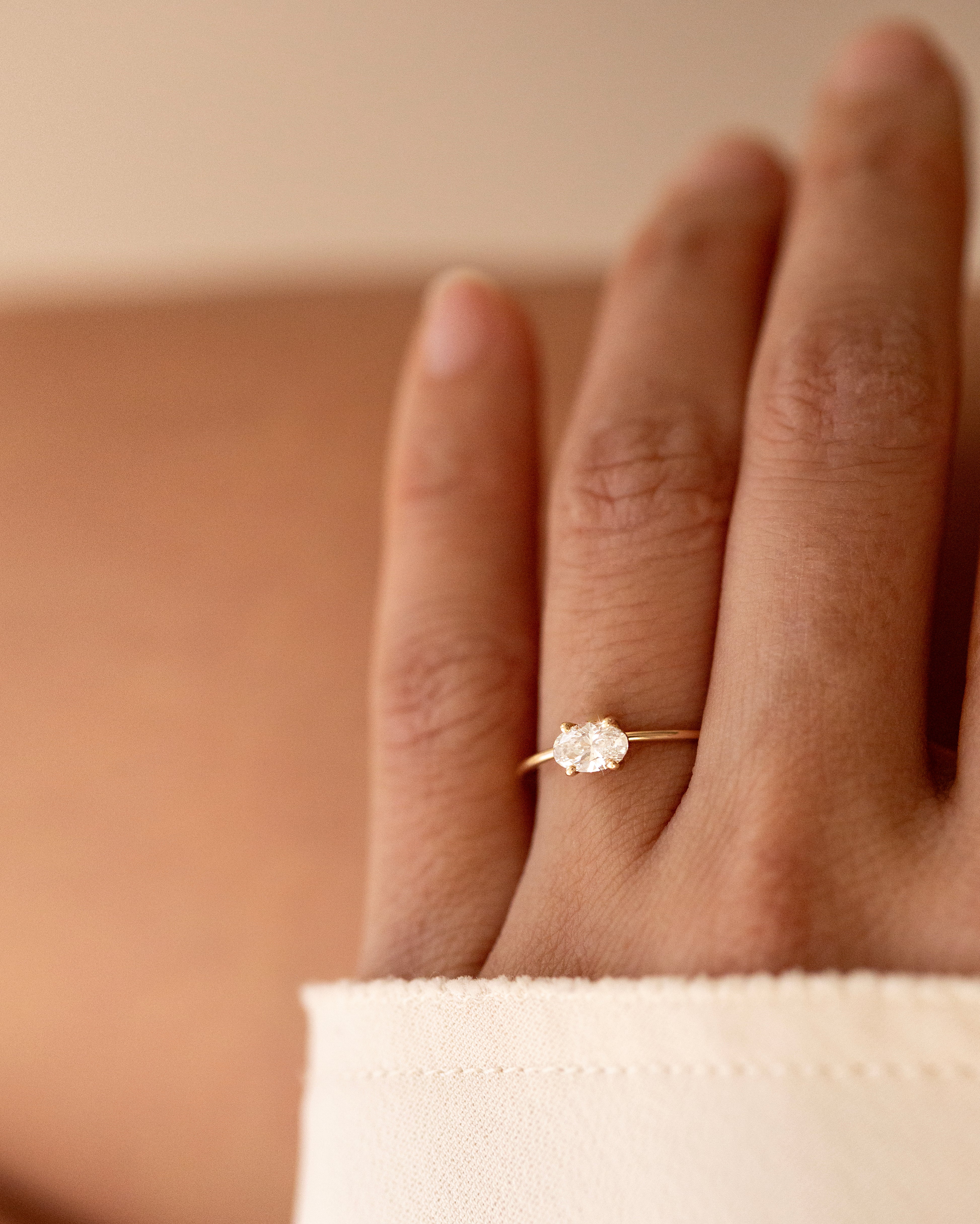 Hand wearing a diamond ring on a neutral background