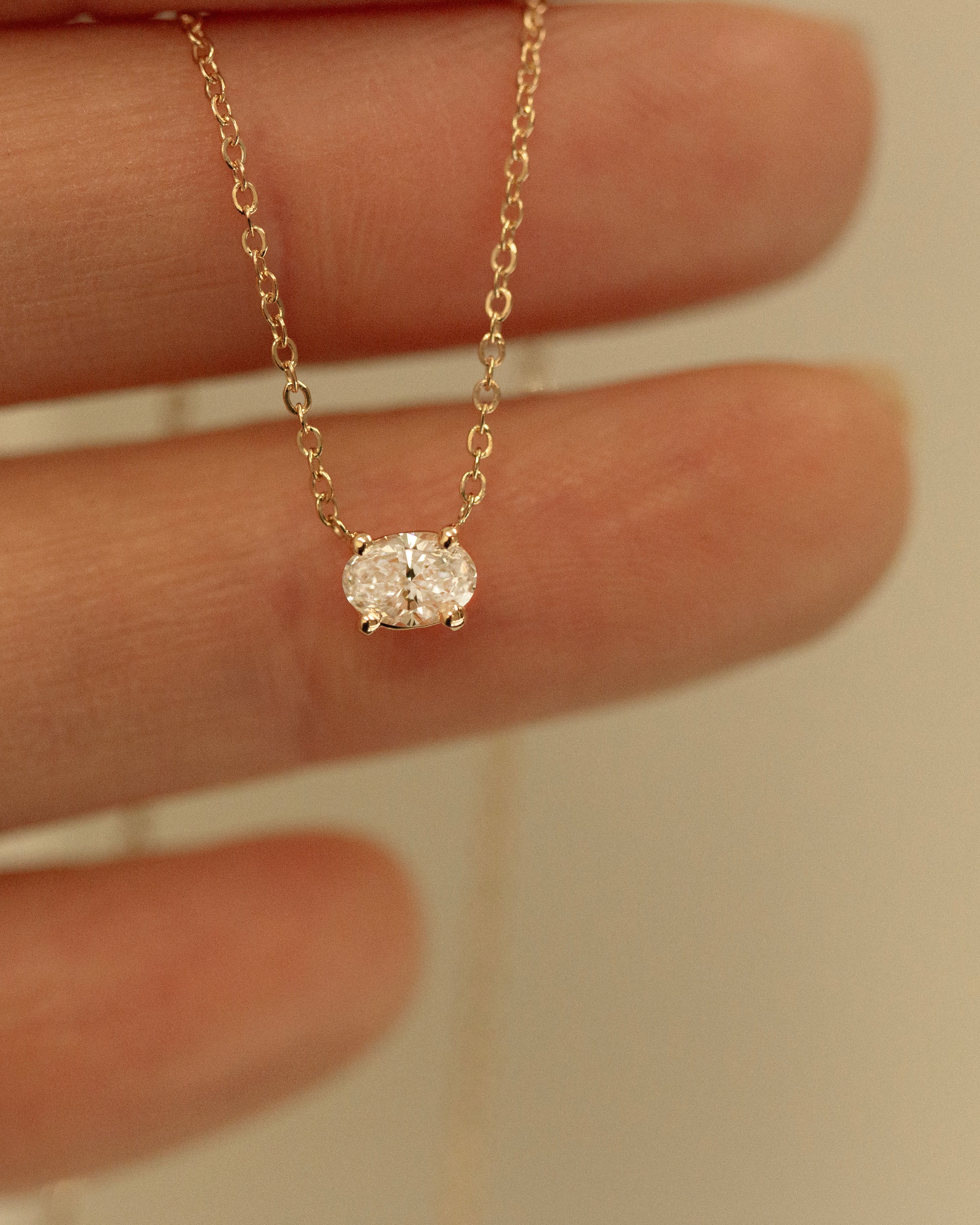 Gold necklace with a small diamond pendant held between fingers against a neutral background
