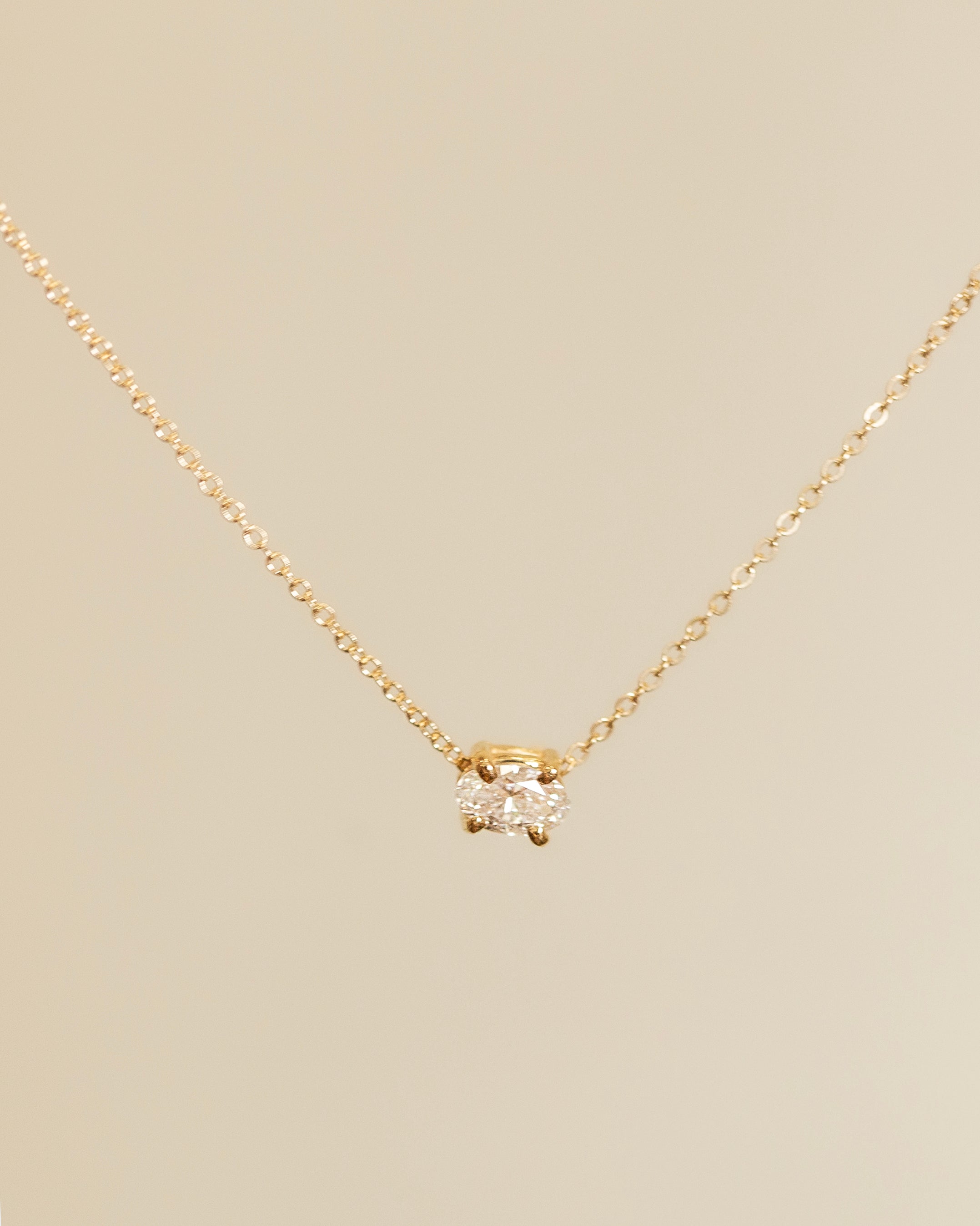 Gold necklace with a diamond pendant on a beige background