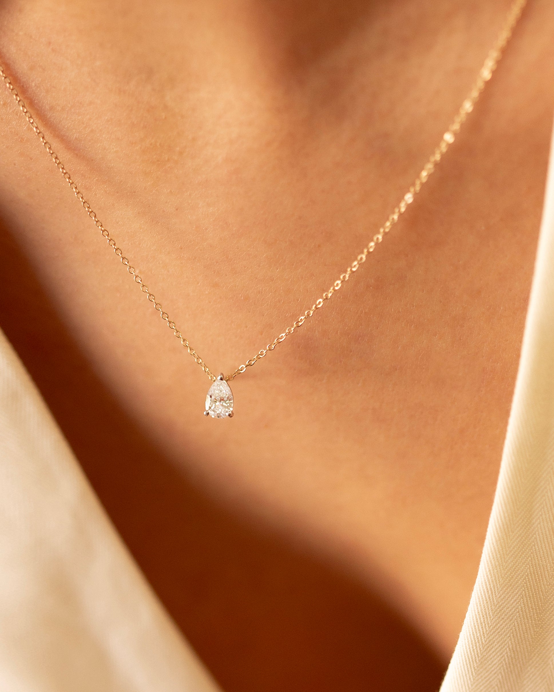Gold necklace with a teardrop-shaped diamond pendant on a soft beige background
