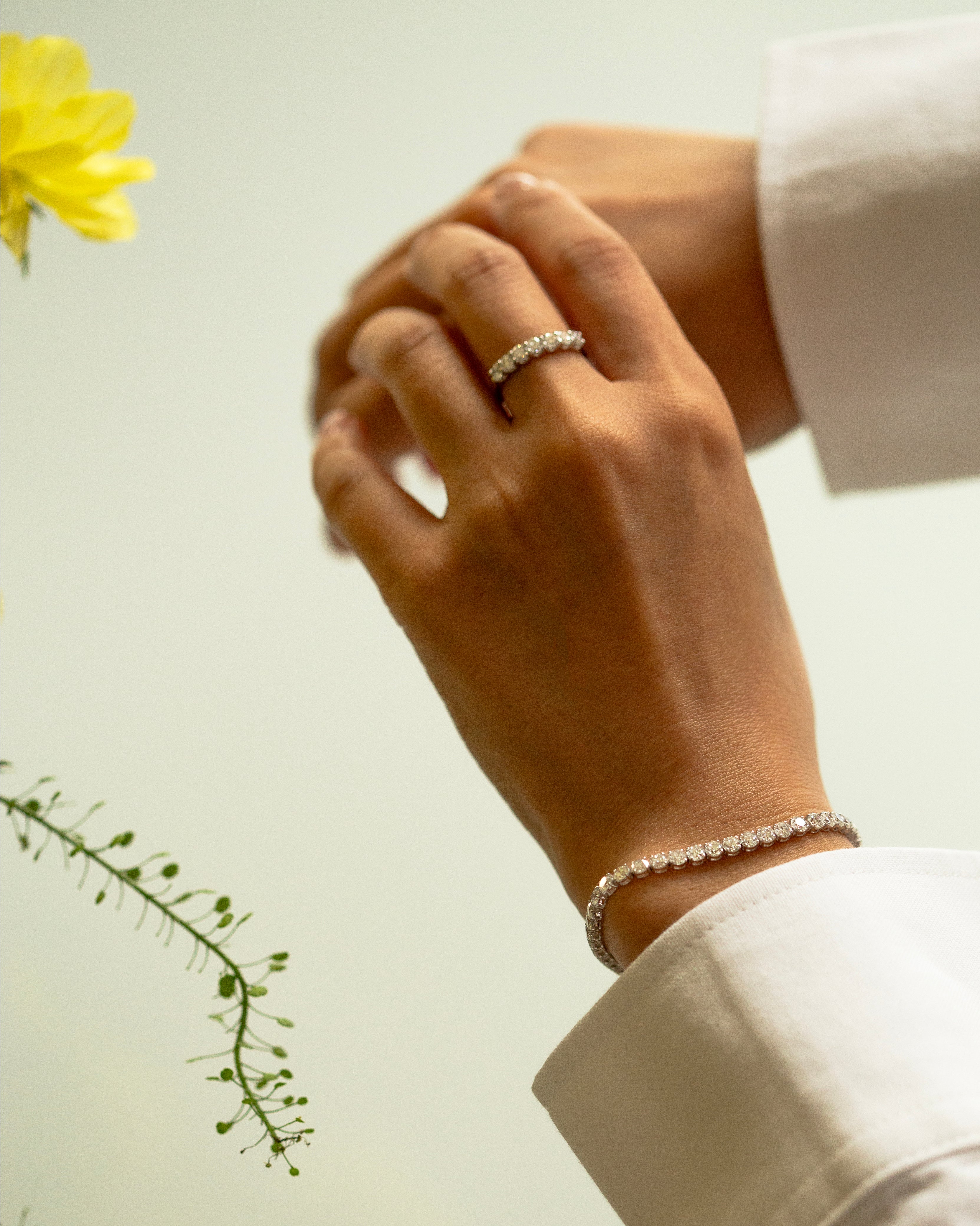 Hand wearing a diamond ring and bracelet with a yellow flower in the background
