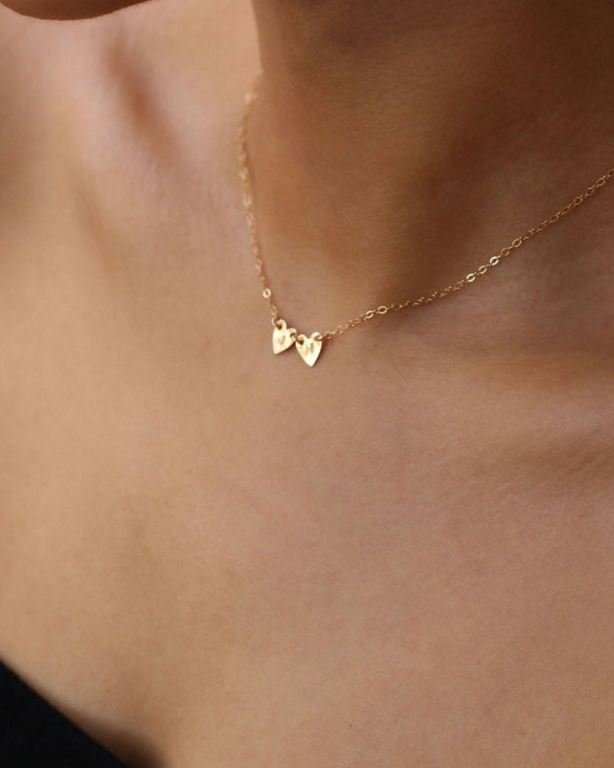 A gold chain necklace with two small heart pendants.